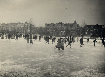 83070 Gezicht op de dichtgevroren vijver in het Wilhelminapark te Utrecht, met schaatsende mensen. Op de achtergrond de ...